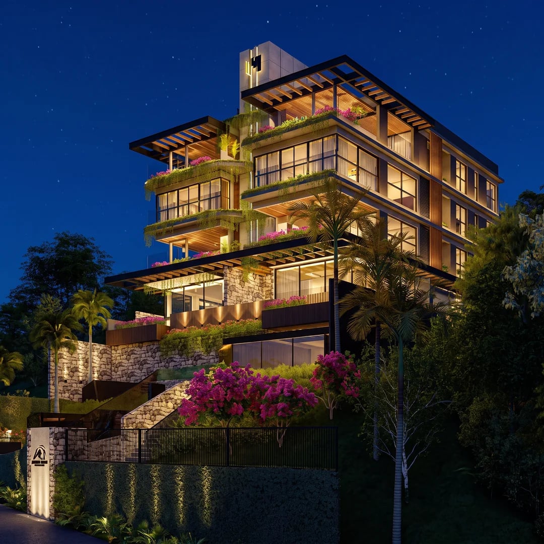 Edifício residencial em encosta arborizada, à noite, com terraços ajardinados iluminados.